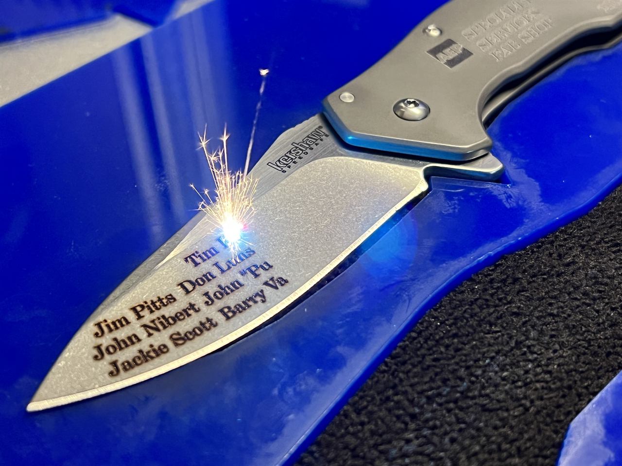 A Kershaw knife blade being laser-engraved with names, sparks flying